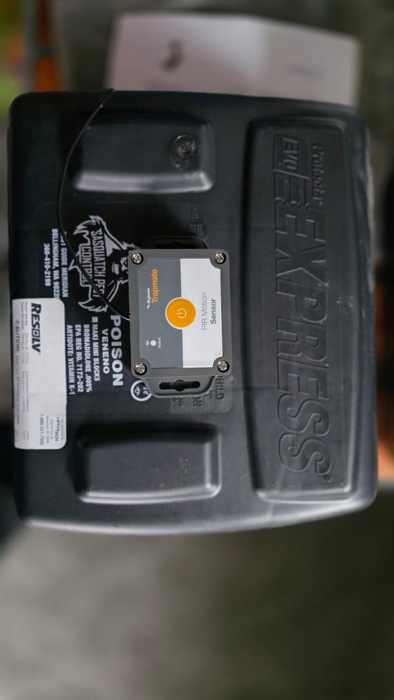 A black tamper-resistant rodent bait station with the company label, fitted with a Skyhawk Trapmate motion sensor on its lid