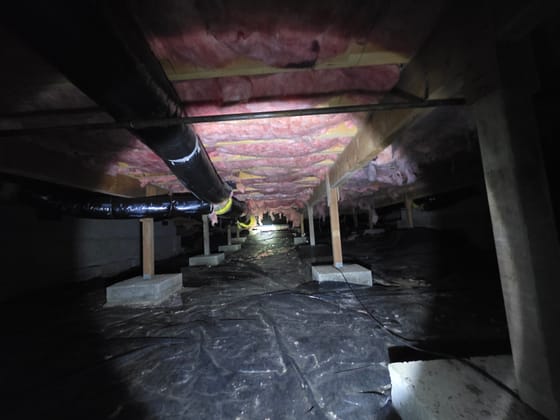 A long crawlspace with insulation between the joists, wrapped ductwork, posts on concrete piers and a black vapor barrier across the ground