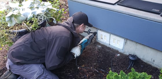 Evan Friese drilling anchor holes in a concrete foundation around a crawlspace vent with a hammer drill
