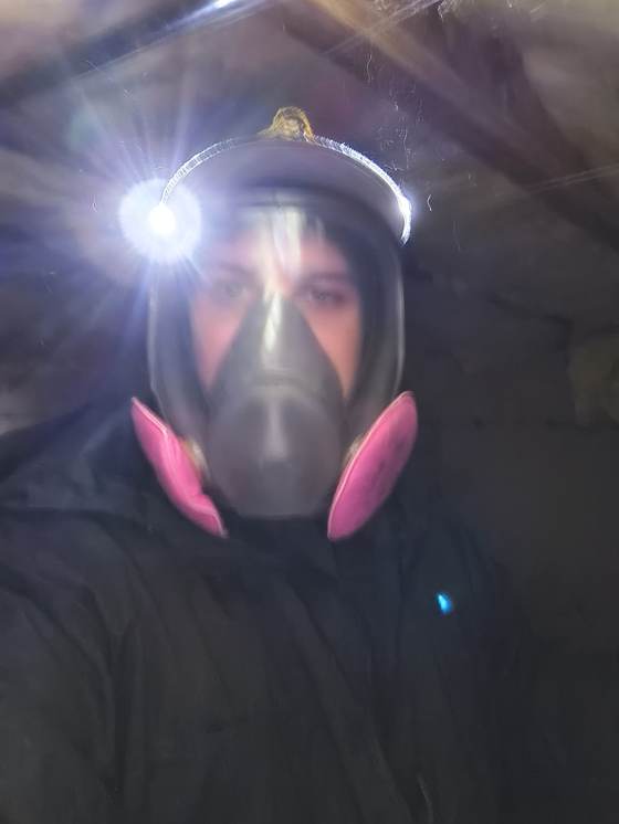 A technician in a full-face respirator with pink filters and a headlamp, ready for crawlspace work