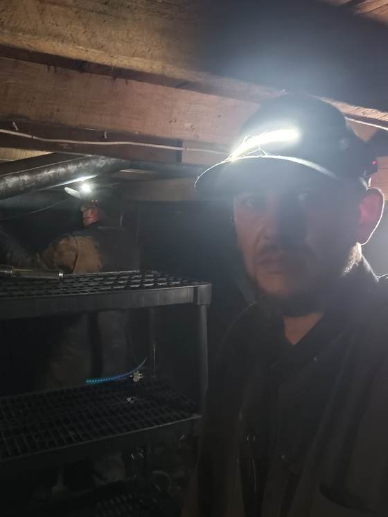A technician working by headlamp in a dark crawlspace