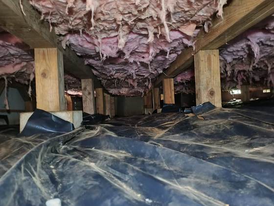 A crawlspace with subfloor insulation and ductwork above a vapor barrier