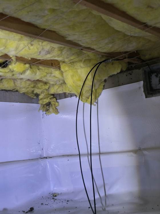 Torn insulation hanging beside wiring in a crawlspace