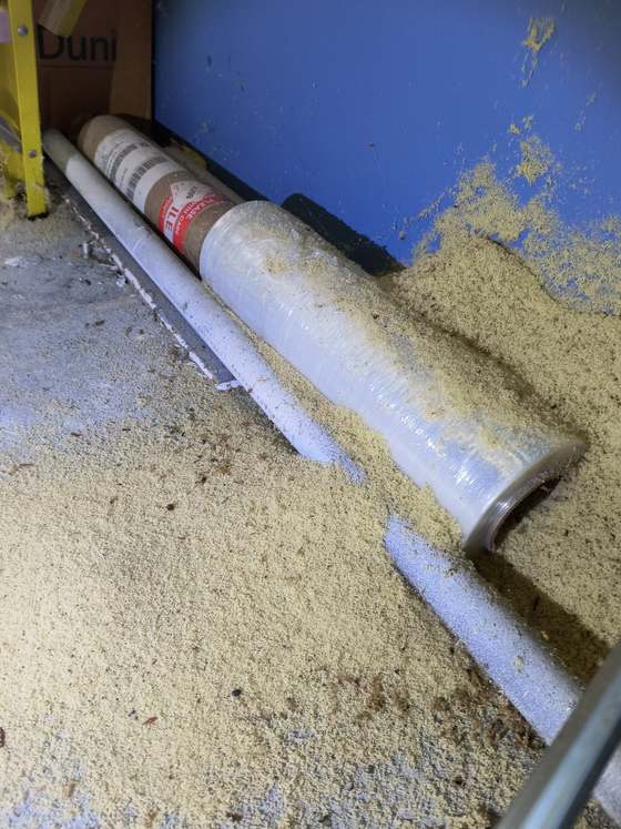 Deep drifts of pale carpenter ant frass banked along a blue warehouse wall, burying the ends of stored rolls and the floor around them