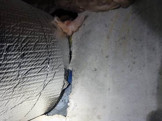 A foil-faced insulated duct pressed against a concrete foundation wall, a gap between them and fiberglass above