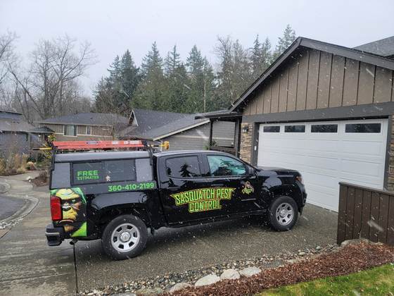A wrapped truck parked in a driveway beside garages during a service visit