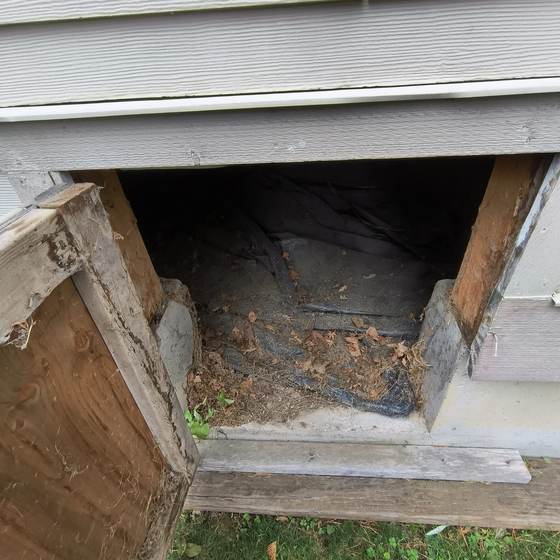 A damaged crawlspace door and dark access opening at a home