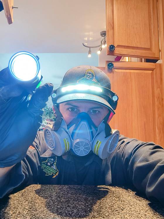A technician wearing a respirator and headlamp for crawlspace work
