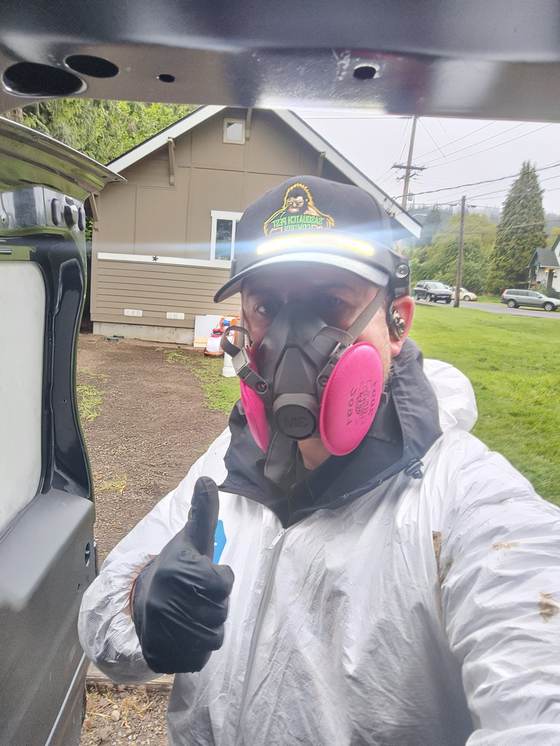 Kristofer Elling in a white protective suit and a half-face respirator with pink filters, giving a thumbs up at the open van