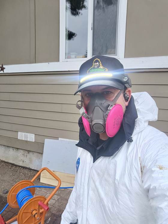 Kristofer Elling in a protective suit and respirator beside the sprayer rig and hose reel at the side of a house