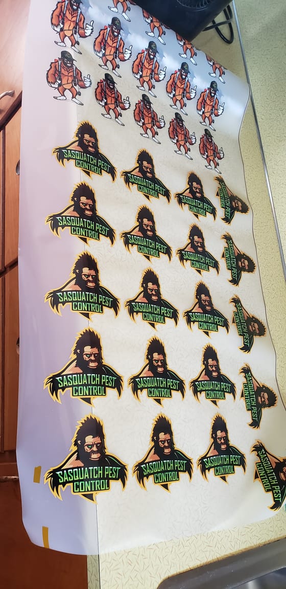 A sheet of freshly printed Sasquatch Pest Control logo transfers and mascot stickers laid out on a counter