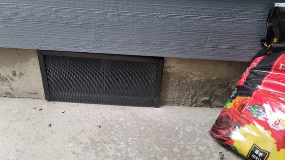 Close-up of a black heavy-gauge mesh screen framed over a crawlspace vent in a concrete foundation