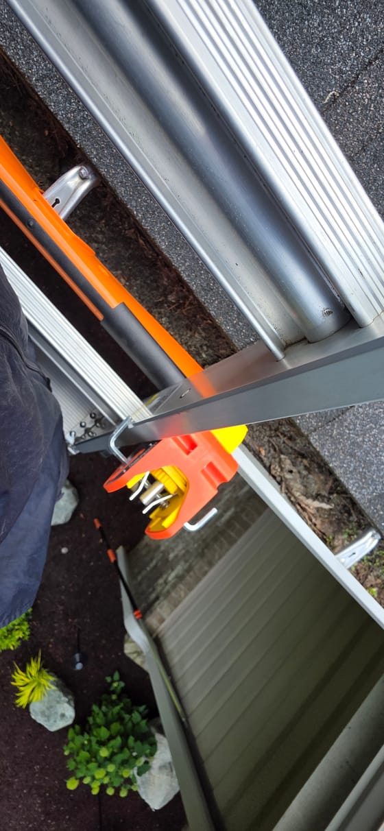 Looking down the top of a ladder: an anti-slip bracket resting on the gutter to protect it, and a lock clamping the ladder in place