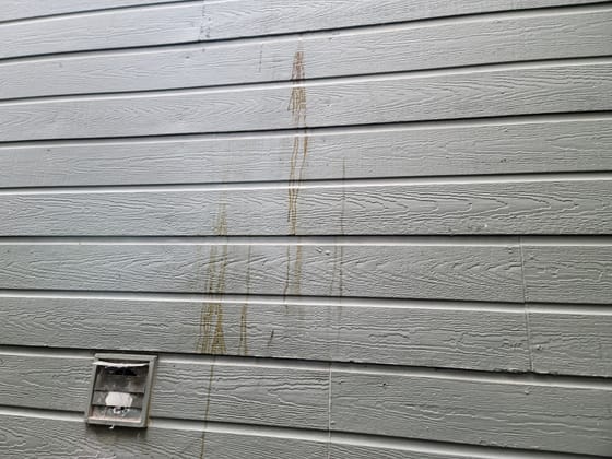 Brown streaks of water staining running down several courses of gray lap siding above a dryer vent