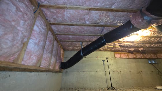 A finished crawlspace with new insulation between the joists and in the framed wall, and a newly wrapped black duct crossing overhead