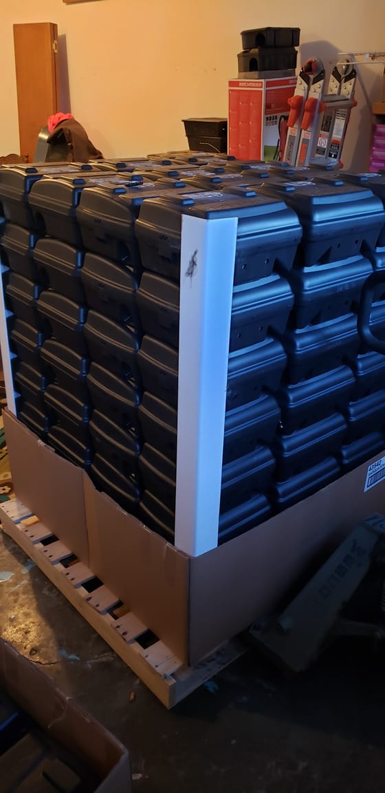 A pallet stacked high with new black tamper-resistant rodent bait stations, delivered to the shop