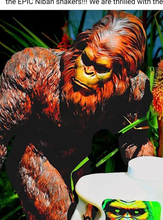 A Sasquatch statue crouched in tall grass and red-hot poker flowers beside a Niban bait shaker wearing the company label