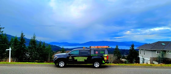 The wrapped Chevrolet Colorado on a hillside street above Bellingham, the bay and the San Juan Islands behind under a stormy sky