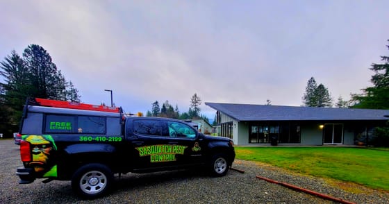 The wrapped Chevrolet Colorado parked on gravel beside a low community building and lawn in Alger under a gray sky