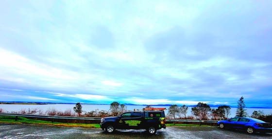 The wrapped Chevrolet Colorado at a pullout on Chuckanut Drive, Samish Bay and distant islands under a wide cloudy sky