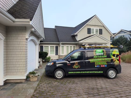 The wrapped service van on a brick driveway in front of a shingled house with dark shutters in Bellingham