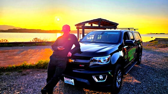 Evan Friese leaning on the wrapped Chevrolet pickup after a long day, the sun setting over the bay on Lummi Shore Road