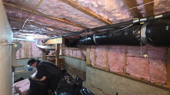 A technician with a headlamp bagging offcuts in a crawlspace after new insulation was installed in the floor joists and the framed walls