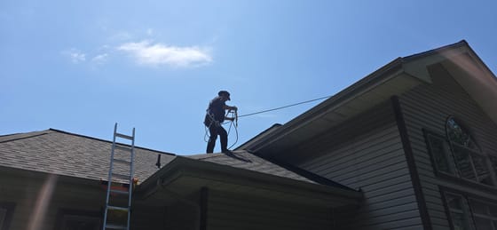 A technician on a roof in a full safety harness, paying out a tied-off rope line in Cougar Paws roofing boots, against a clear sky