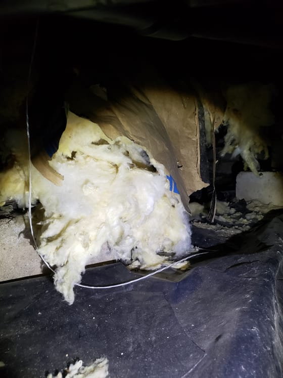Kraft-faced yellow insulation torn open and hanging from a crawlspace joist, the paper facing ripped