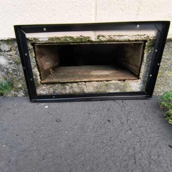 The steel frame of a vent guard screwed to the foundation around an open crawlspace vent, the timber lintel visible inside
