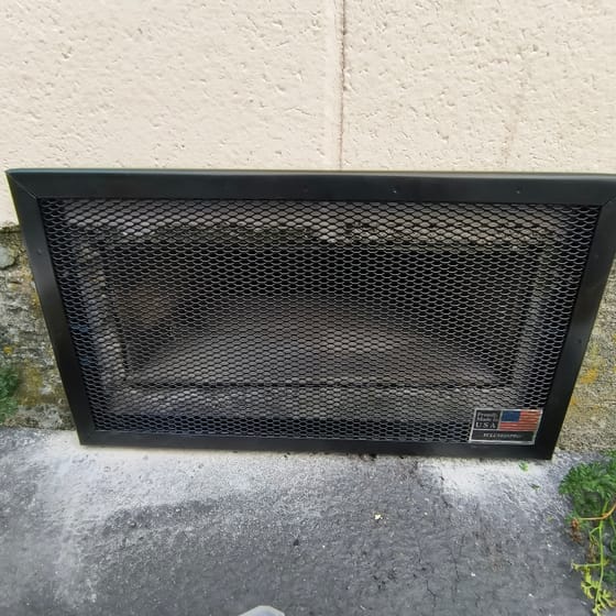 The finished vent guard, heavy black mesh in a welded steel frame, fitted over the foundation vent of a restaurant