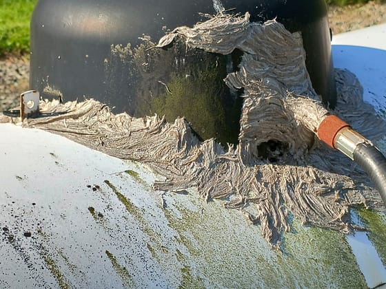 Close-up of gray yellowjacket nest paper spread over the valve and hose fitting of a white propane tank, with the entrance hole visible
