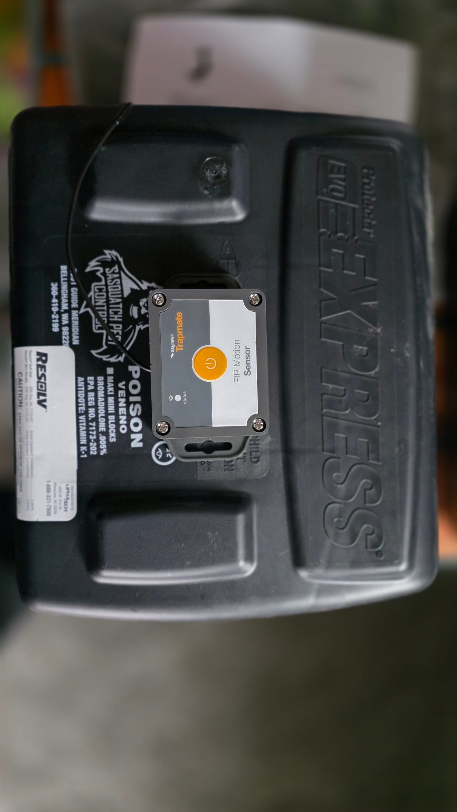A black tamper-resistant rodent bait station with the company label, a small white Skyhawk Trapmate sensor fitted to its lid