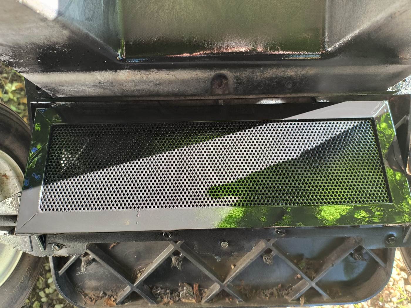 A perforated metal screen in a folded steel frame fitted over a foundation vent opening, seen from outside at ground level