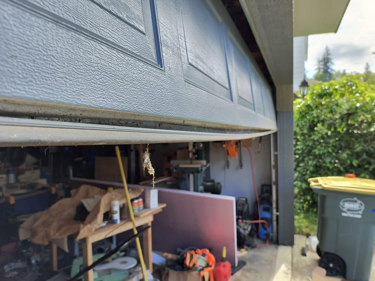 The bottom edge of a raised garage door with bare metal where the seal has gone, and daylight showing along the gap beneath it