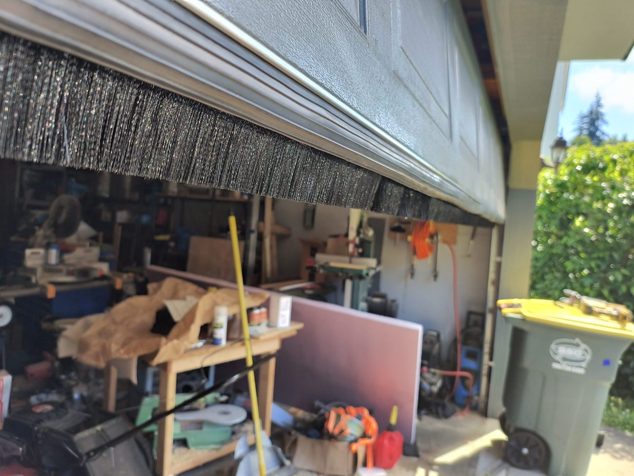 The same garage door fitted with an Xcluder rodent-proof bottom seal, a rubber gasket with a brush strip behind it, closing the gap