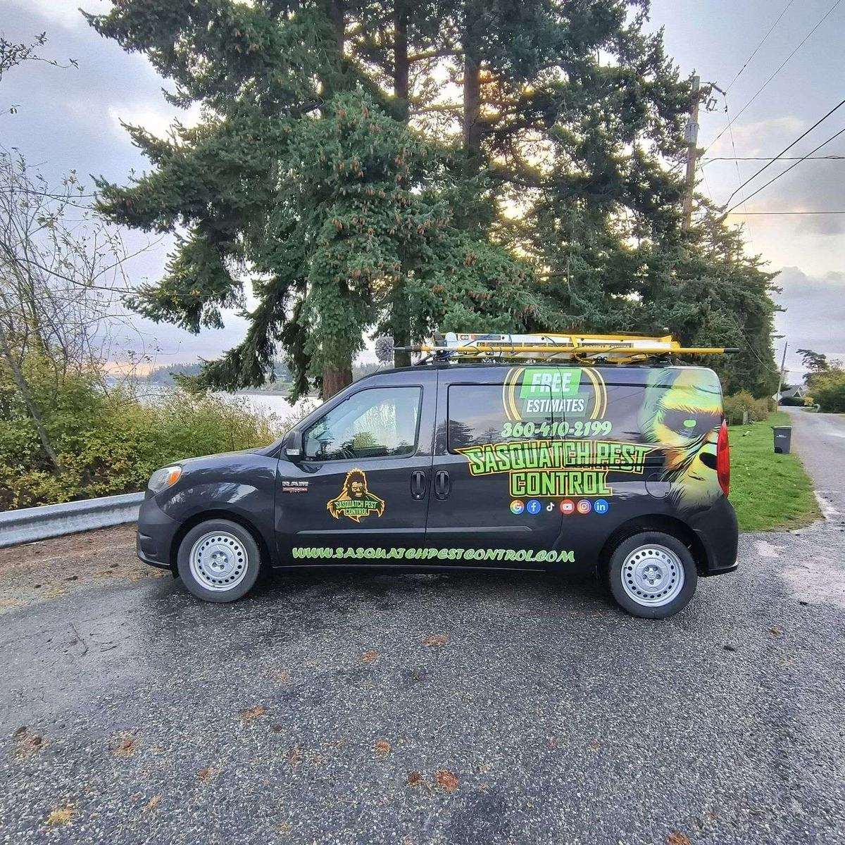 A wrapped Sasquatch Pest Control van parked on a wet driveway lined with tall evergreens