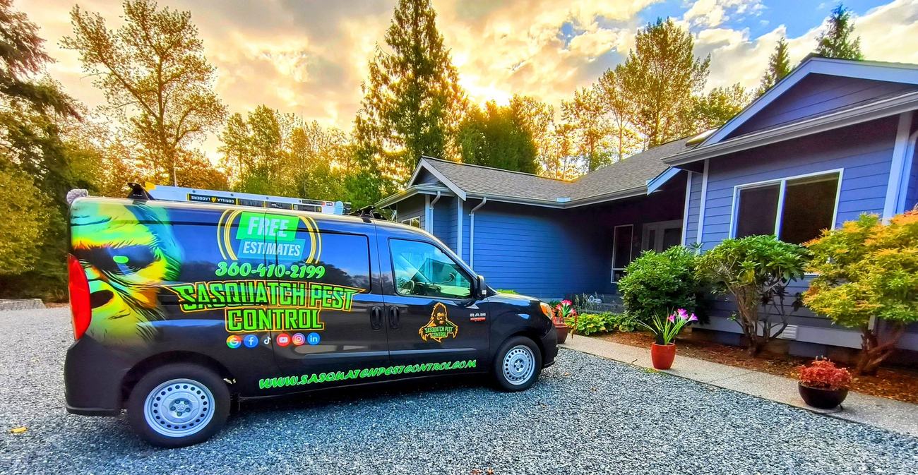 A wrapped service van parked on the gravel drive of a blue single-story home under an autumn sky