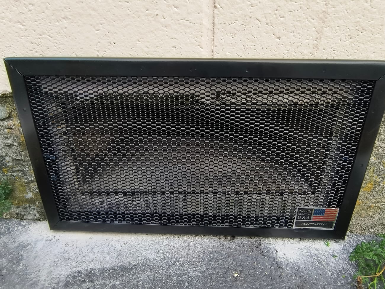 The same opening fitted with a black steel vent guard, heavy mesh in a welded frame screwed to the foundation